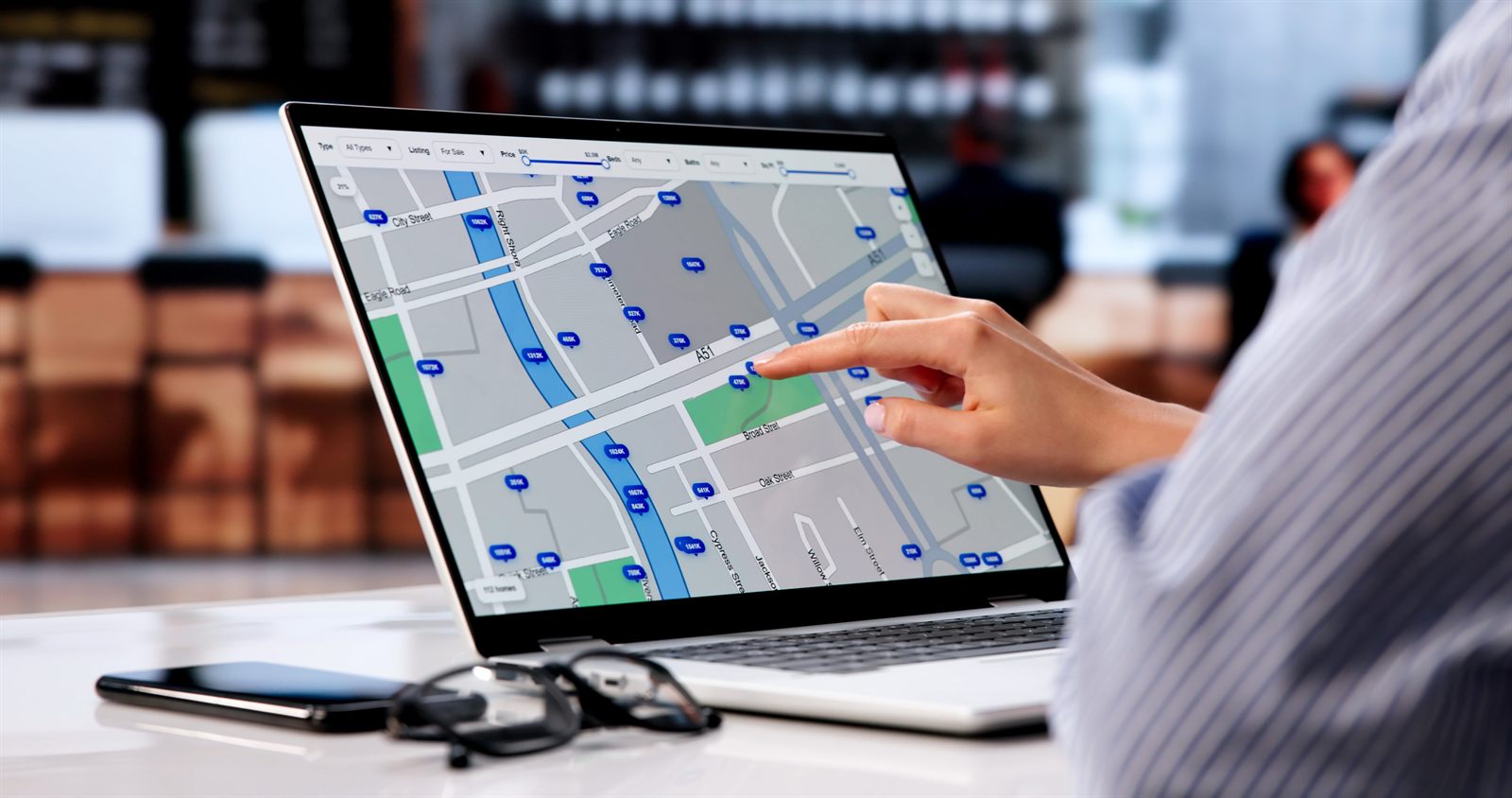 Traveler pointing at a city map on a laptop screen beside a phone and sunglasses