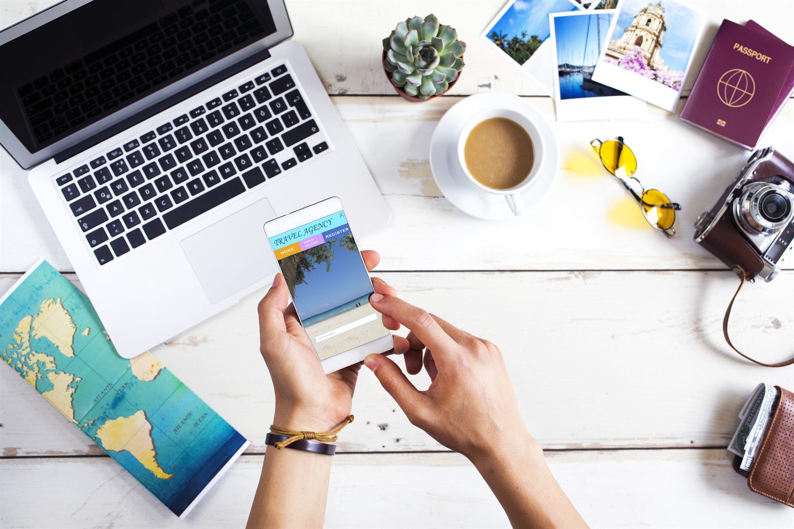 Overhead view of a laptop, passport, map, camera and coffee on a white desk